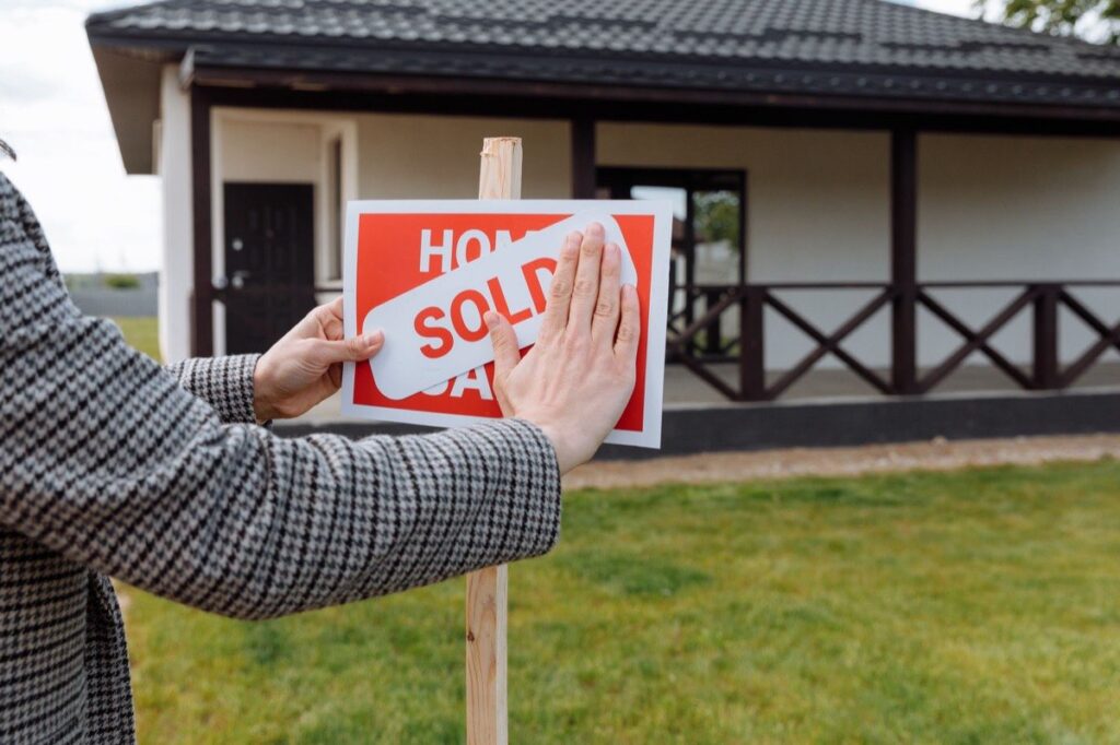 Real estate agent placing a SOLD sticker on a home-for-sale sign
