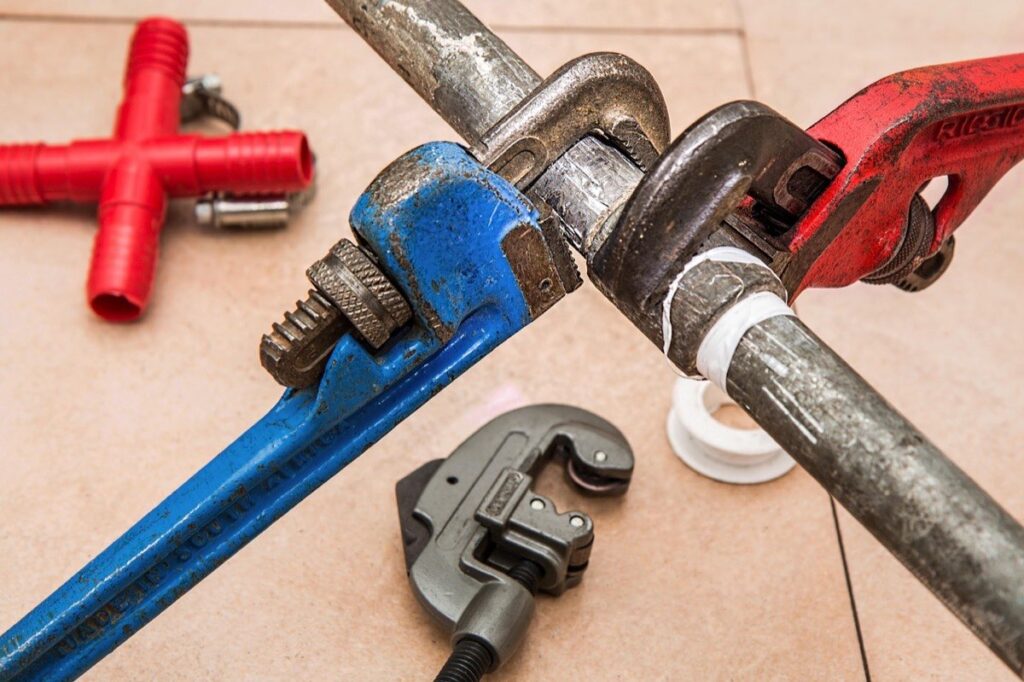 Two pipe wrenches gripping a water pipe during an emergency plumbing repair